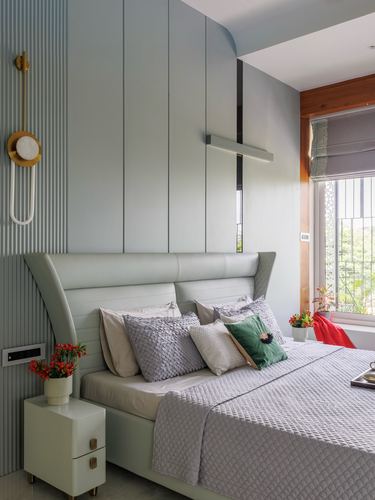 Sage green bedroom with fluted paneling, curved upholstered headboard, and layered grey pillows near a window