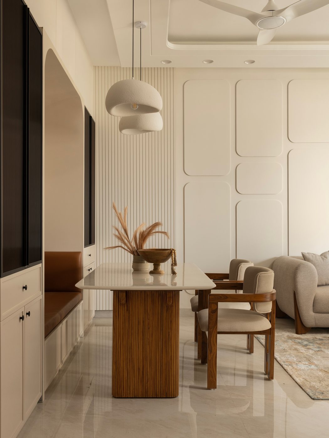 Neutral dining nook with fluted wood table, cane pendant light, and banquette seating beside living room