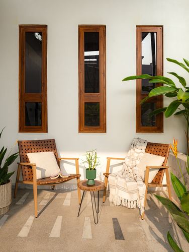 Two woven lounge chairs and a small side table on a stone balcony beneath three tall narrow windows.