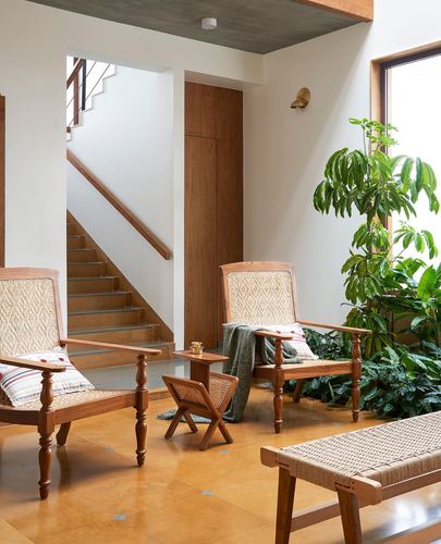 Living room with cane armchairs, wooden staircase, indoor plant and terracotta flooring