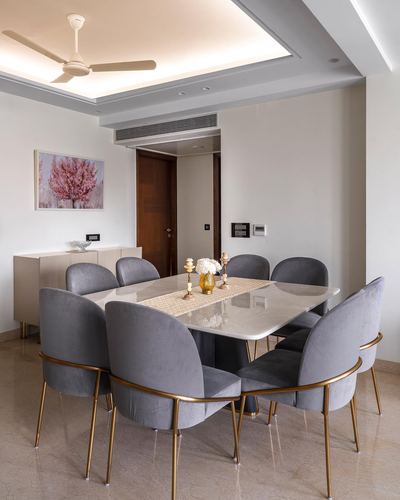 Dining room with marble table, eight grey velvet chairs with gold legs, and cove-lit coffered ceiling