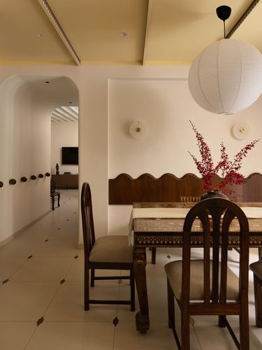 Dining area with carved wood chairs, scalloped wood paneling, red branch centerpiece, and arched hallway beyond