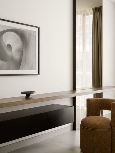 Minimalist living room corner with floating wood console, black cabinet, and mustard bouclé chair by a curtained window