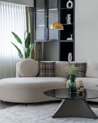 Curved beige sofa with an arc brass lamp beside a dark glass display cabinet and oval coffee table