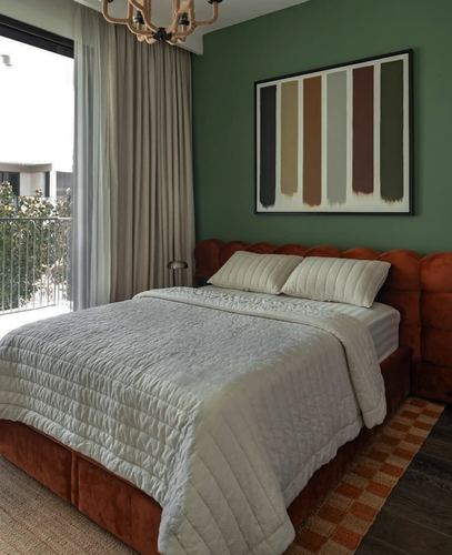 Bedroom with sage green wall, rust velvet tufted bed, striped artwork, and balcony view
