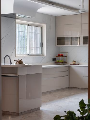 Modern L-shaped kitchen with glossy beige cabinets, marble backsplash, and a central island under a sliding window
