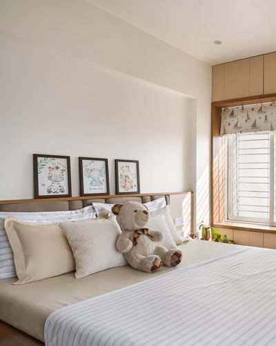 Child's bed with teddy bear and cushions below three framed animal prints near sunlit window