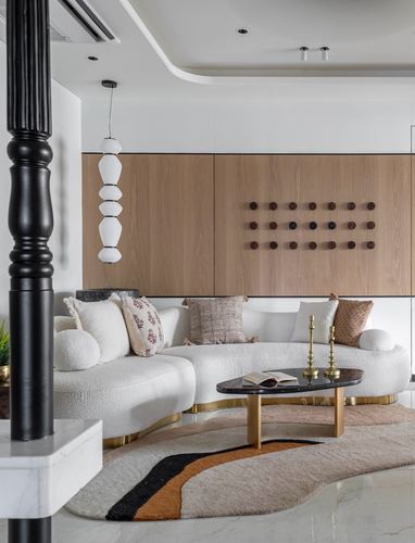 Curved white boucle sofa with wooden paneled wall and layered pendant light in a Pune living room