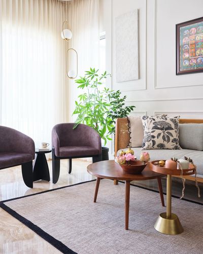 Living room with cane sofa, mauve velvet chairs, wooden coffee table and framed art on paneled walls