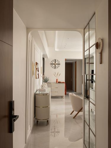 View through arched doorway down a marble corridor to a fluted console with clock and accessories