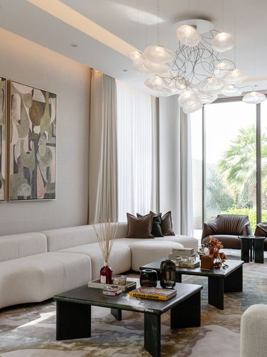 Double-height living room with beige sectional, dark stone coffee tables, and cloud-like chandelier