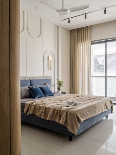 Bedroom with grey upholstered bed, arched panelled wall, and large window with sheer curtains