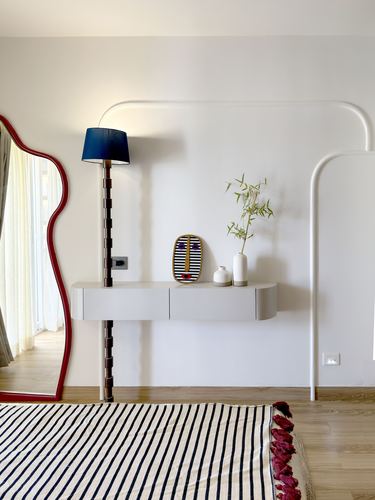 Floating console with lamp and mirror against curved white wall, striped rug on wood floor