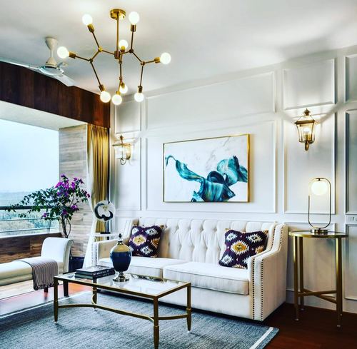 White paneled living room with tufted sofa, brass chandelier, and abstract art above