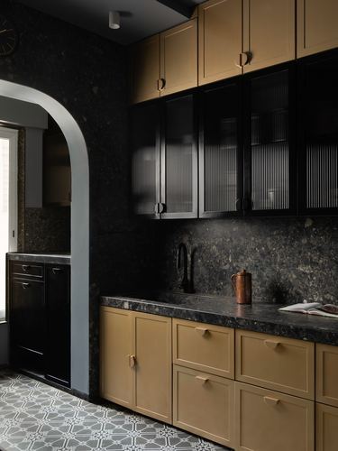 Dark stone kitchen with mustard cabinetry, black fluted upper cabinets, and an arched doorway