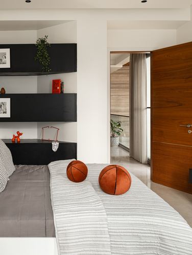 Bedroom with black floating shelves, orange basketball cushions, and view through wooden door to stone corridor
