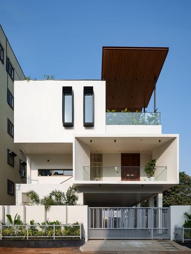 White multi-storey house facade with cantilevered wood-clad canopy and glass terrace over entry