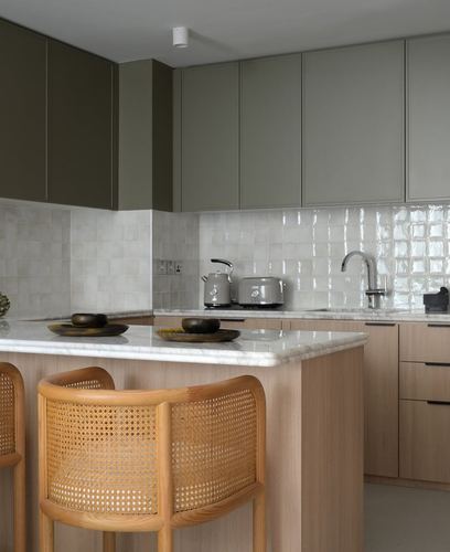 Kitchen island with cane stools, marble counter, olive and wood cabinetry, tiled backsplash