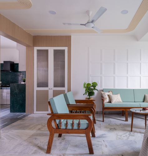 Living room with sage green sofa, teak armchairs, cane door, and marble flooring in Pune apartment
