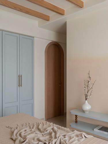 Bedroom corner with arched wood door, blue wardrobe, and floating shelf holding a vase.