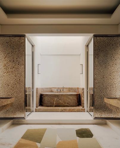Symmetrical bathroom framed by glass doors and textured stone walls, revealing a veined stone bathtub in an inner alcove