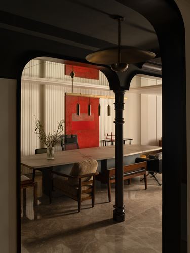 View through a black arched column into a dining room with red artwork and pendant lights