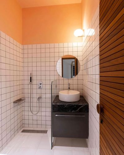 Small bathroom with orange upper wall, white square tile, round mirror and dark stone vanity