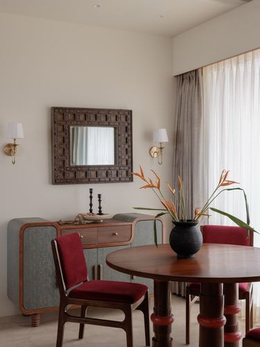 Dining nook with round wood table, red velvet chairs, and a carved antique mirror above a patterned sideboard