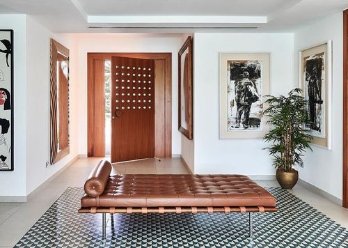 Entry hall with studded wood door, tan leather daybed on patterned tile, and framed art
