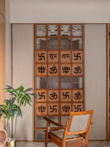 Carved wooden door with Om and swastik motifs beside a cane armchair and potted plant