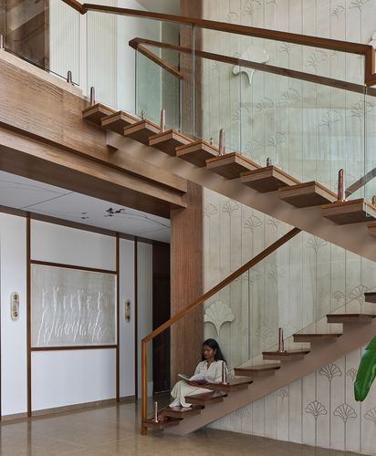 Woman reading on a floating wooden staircase beside a textured stone wall with glass railing