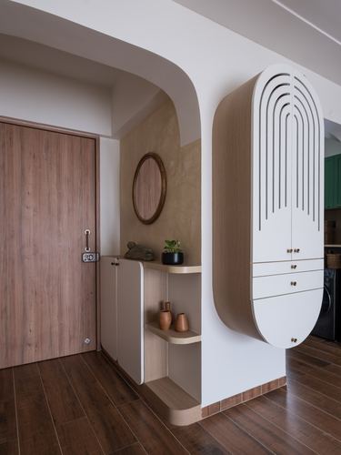 Entryway with arched niche, round mirror, wooden door, and curved fluted cabinet in warm tones