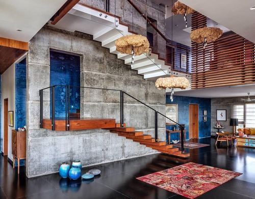 Double-height foyer with wooden floating staircase, concrete wall, blue accent wall, and cocoon pendant lights