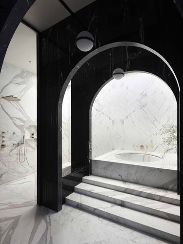 Nested black and white marble archways leading to a sunken marble bathtub lit from above