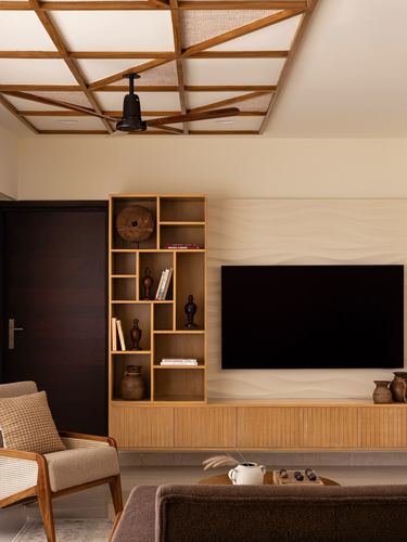 Living room with wooden ceiling grid, open shelving, wave-textured wall and wall-mounted TV