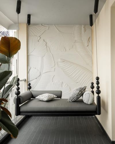 Black hanging daybed with grey cushions before a carved leaf-relief wall on a balcony