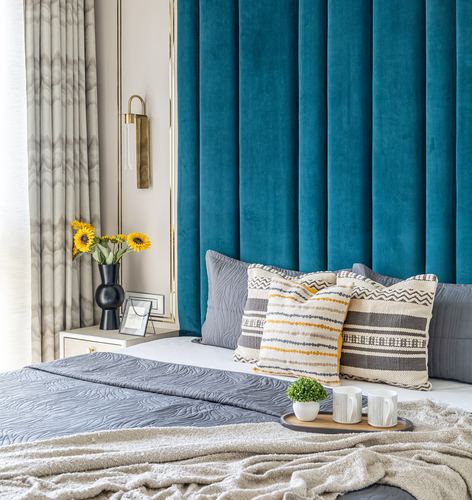 Bed with teal velvet channel headboard, grey and mustard patterned cushions, sunflowers on nightstand