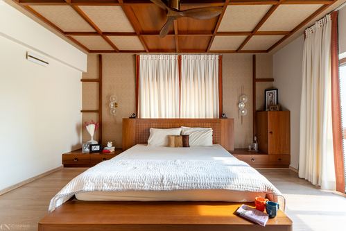 Wood-paneled bedroom with coffered ceiling, platform bed, and rust-trimmed curtains in daylight