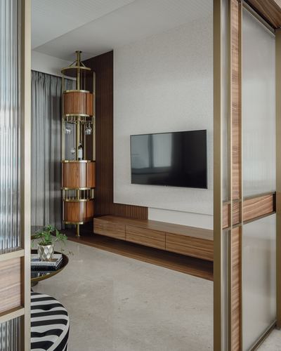 Living room with wall-mounted TV, walnut console, and cylindrical brass bar cabinet seen through fluted glass door