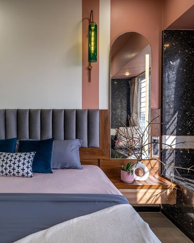 Bedroom corner with grey channel-tufted headboard, arched mirror, and dark stone wall
