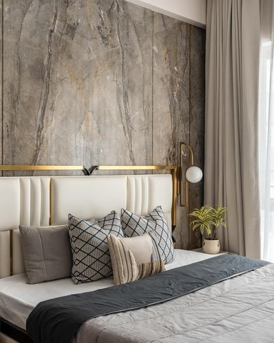 Bed with cream tufted headboard against grey-brown stone wall and brass sconce