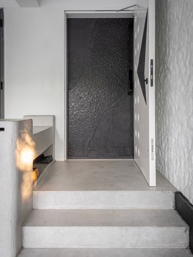 Entry foyer with concrete steps leading to a textured black door and grey plaster walls