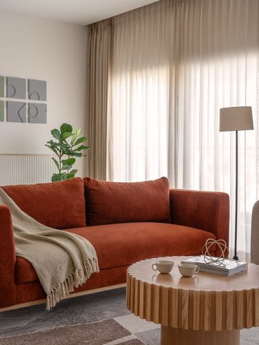 Terracotta velvet sofa beside sheer curtained window with round fluted wood coffee table