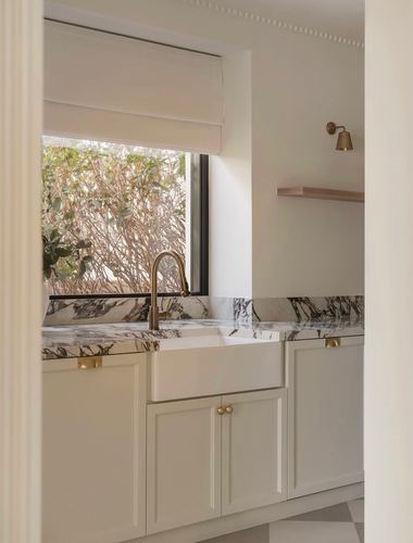 Kitchen sink with brass faucet and veined marble backsplash seen through an arched doorway