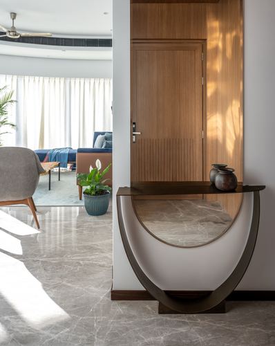 Entry foyer with curved marble-top console table beside a grooved wooden door, living room visible beyond