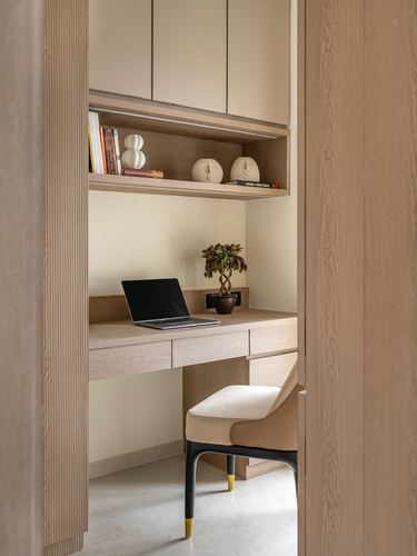Small study nook with wood desk, laptop, plant, and shelving seen through an open wood door