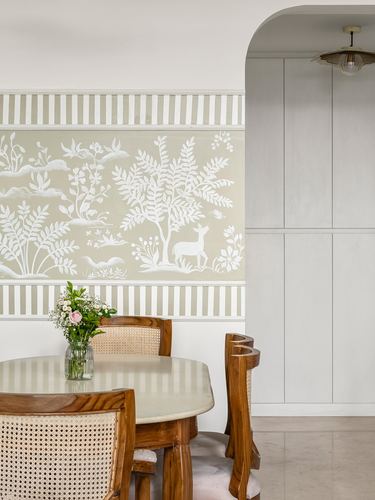 Dining nook with cane chairs, wooden table, and chinoiserie mural beside an arched cabinetry wall