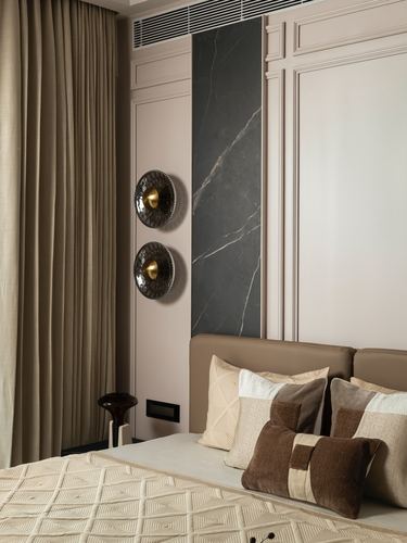 Bedroom corner with taupe leather headboard, layered pillows, marble wall inlay, and sculptural wall sconces.