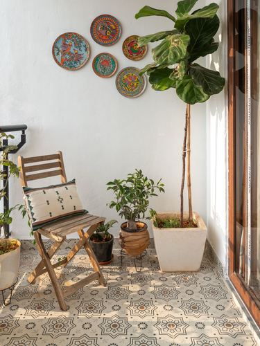 Balcony corner with patterned tiles, folding chair, potted fiddle leaf fig, and wall plates