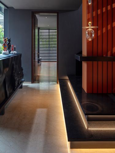 Entry passage with marble floor, black carved console, and glowing red fluted wall panel beyond a stone platform.